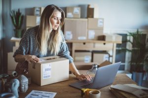 Working woman at online shop. She wearing casual clothing and checking on laptop address of customer and package information