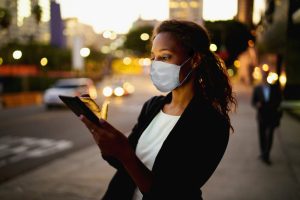 Businesswoman using a digital tablet at night in the city wearing a healthcare mask.